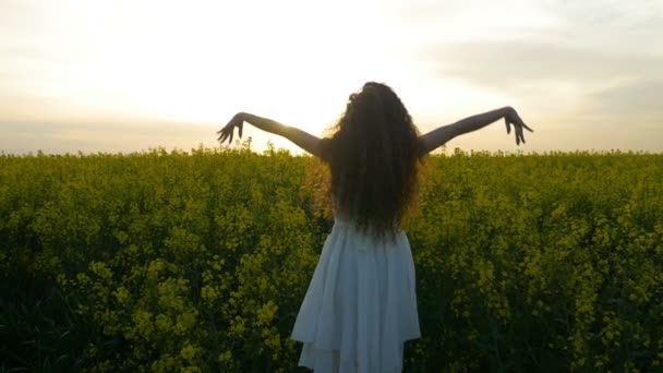 Fiatal parasztlány öltözött fehér spinning a magas repce virágok területén emelt karokkal és békés érzés — Stock videók