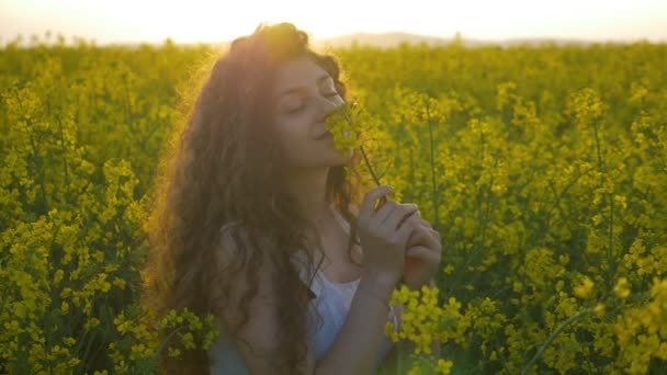 Movimento lento da menina adolescente em vestido branco girando e sorrindo no campo de colza — Vídeo de Stock