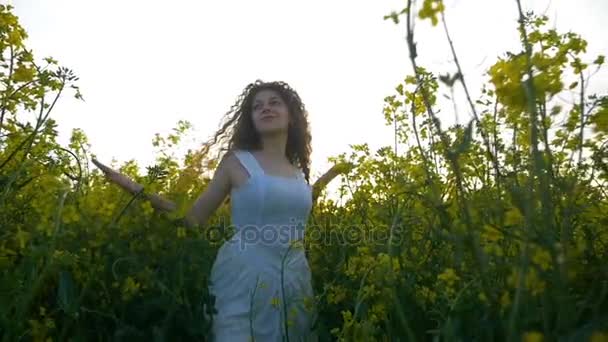 Lento movimento de beleza menina sorridente com cabelos longos desfrutando de uma caminhada de verão no campo rural de plantas de canola — Vídeo de Stock