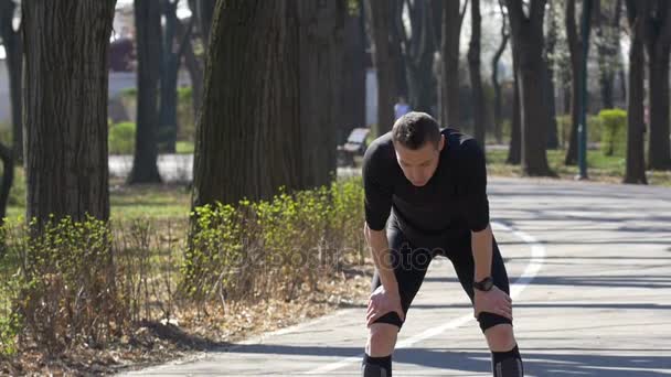 Il rallentatore del jogger maschile in forma dopo una breve pausa riprende a respirare correndo nel park setting smartwatch tracker — Video Stock