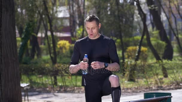 Rallentamento del jogger esausto che beve acqua dalla bottiglia dopo aver terminato il suo allenamento nel parco — Video Stock