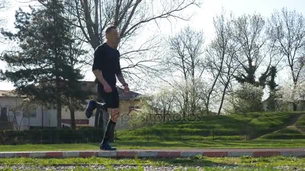 Атлетик делает упражнения на ногах в парке и разогревается перед забегом утром — стоковое видео