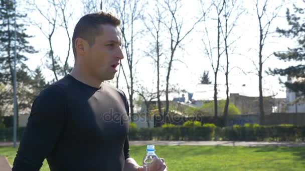 Joggeur fatigué en vêtements de sport boire de l'eau de bouteille en plastique après marathon dans le parc — Video