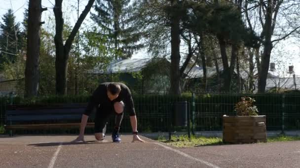 Hombre atleta jogger en ropa deportiva a partir de correr desde la posición de inicio bloque al aire libre o una pista de atletismo — Vídeos de Stock