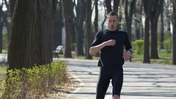 Ajuste corredor corriendo en el parque tomando un descanso y establecer su reloj inteligente rastreador de fitness — Vídeos de Stock