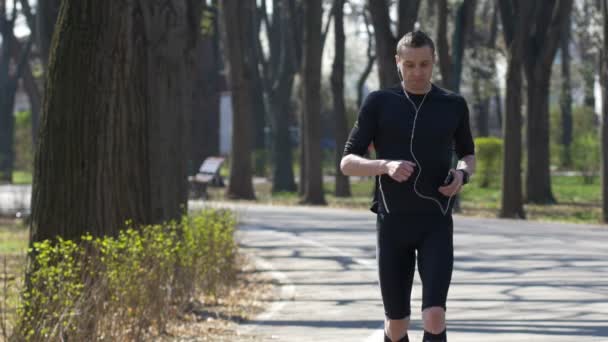 Atleta profesional con smartphone y manos libres revisando rastreadores de fitness mientras descansa — Vídeos de Stock