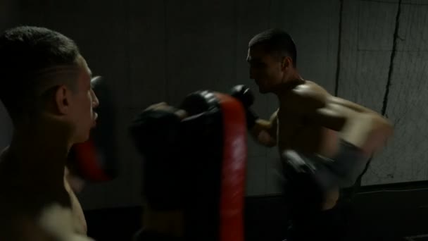 Movimiento lento de los jóvenes deportistas que entrenan en el gimnasio para el partido de kickboxing usando almohadillas de perforación tailandesas — Vídeo de stock