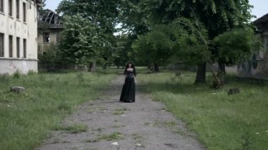 Gotik siyah giysiler ve kötü ifade ile eski bir köşkün harap binalar arasında yürüyüş sarmaşık yaprakları bir taç olan korkunç kadın