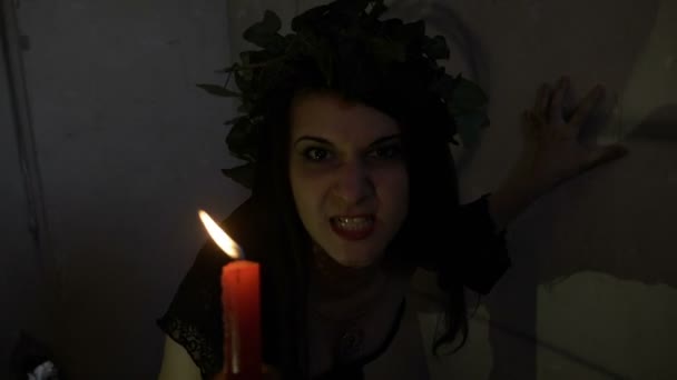 Exorcismo de bruja con el mal desprecio poseído por el demonio vestido de negro gruñendo y sosteniendo una vela en su mano — Vídeos de Stock