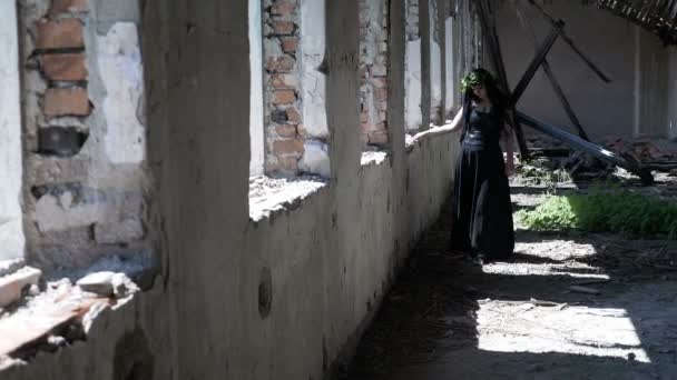 Kontemplativa gotiska häxan flicka går bredvid förstört windows i en gammal förstörda herrgård — Stockvideo