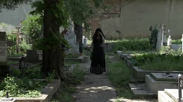 Скорбящая вдова, наполненная горем, покидает усопшего мужа могилу, идя по аллее кладбища — стоковое видео