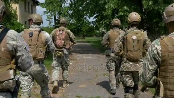 Groupe de soldats portant leur arme patrouillant parmi les arbres et les bâtiments en ruine — Video