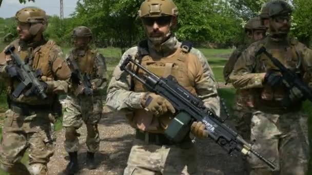 Fechamento da equipe militar andando em uma formação em patrulha fora em uma área rural segurando suas armas — Vídeo de Stock