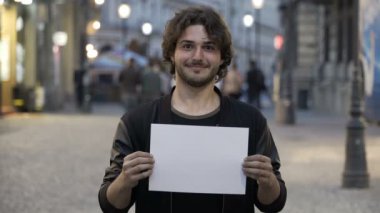 Mutlu gülümseyen genç adam şehirde sokakta bir boş kopya alanı afiş tutarak