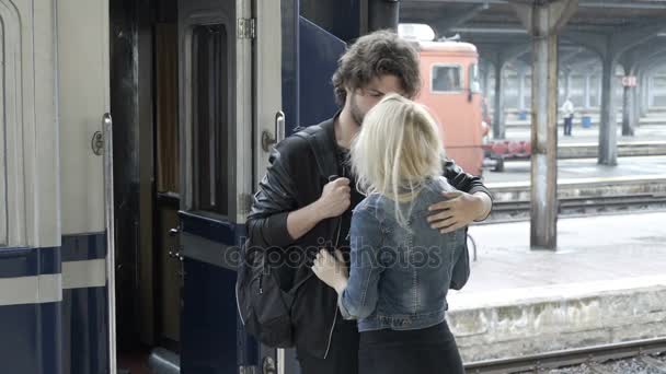 Сумний молодий чоловік у коханні пестить і прощається зі своєю дівчиною на залізничній станції перед від'їздом у дощовий день — стокове відео