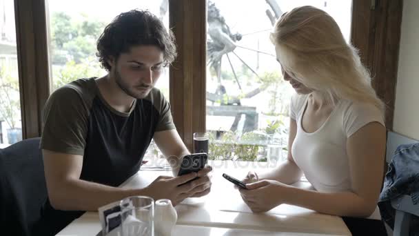 使用して、スマート フォンを見てレストランに座って美しいロマンチックなカップル — ストック動画