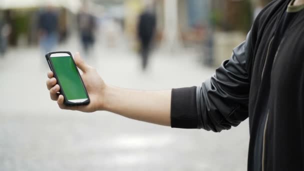 Мужчина, держащий смартфон в общественном парке, касается зеленого экрана хромы ключа — стоковое видео