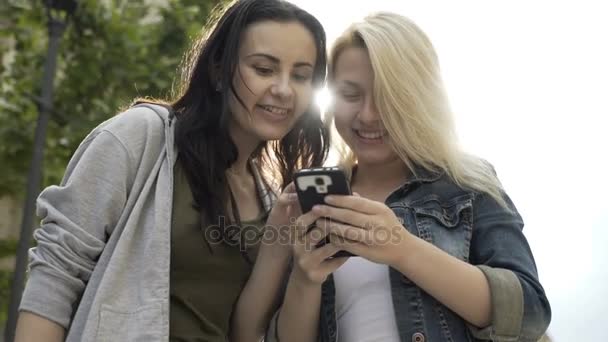 Dos chicas jóvenes riendo y desplazándose pantalla táctil de teléfono inteligente mirando algo divertido en las redes sociales de Internet — Vídeo de stock