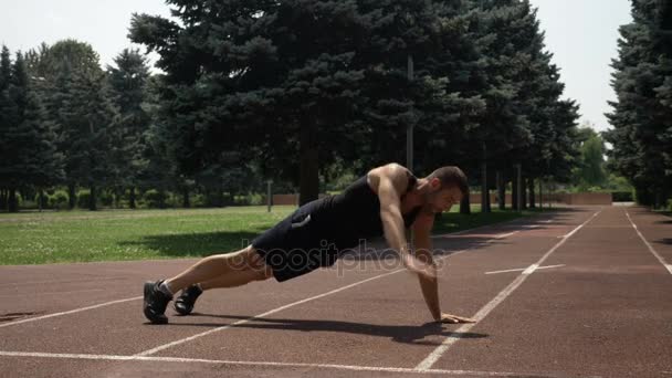 Joven hombre guapo entrenando en pista de atletismo en el parque — Vídeo de stock