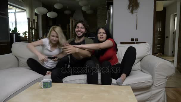 Três amigos discutem sobre o controle remoto em casa na sala de estar e mudam os canais de TV — Vídeo de Stock