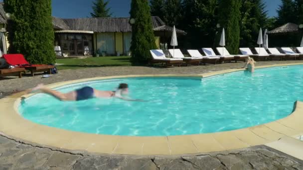 Garçon saute dans l'eau dans la piscine et va nager pendant que la fille le regarde 