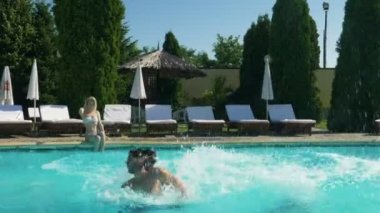 İki adam havuz içine atlamak ve kız üstünde belgili tanımlık kenar ve saatler otururken güzel bir yüzmenin tadını çıkarın