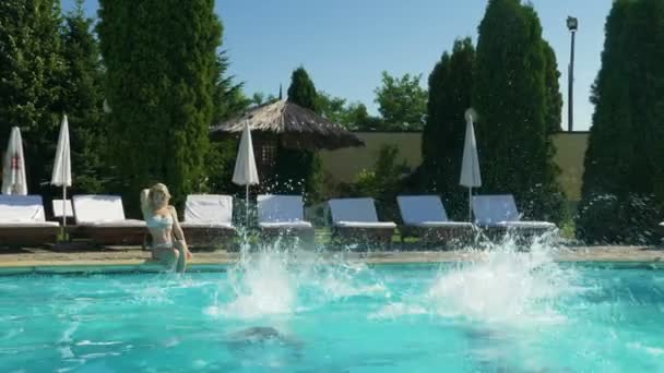 Dos chicos saltan a la piscina y disfrutan de un buen baño mientras la chica se sienta en el borde y observa — Vídeos de Stock