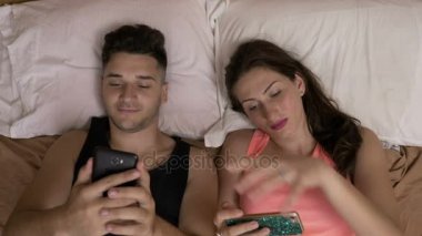 Sevgi dolu ve rahat bir çift yatakta kadın smartphone cep telefonu ile ilginç bir içerik izlerken döşeme