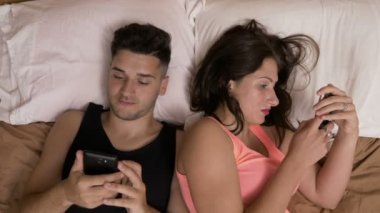 Genç çift yatakta birbirlerini görmezden akıllı telefonlar için bağımlısı sosyal medya sohbet döşeme