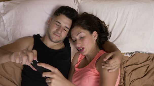 Amar pareja joven pasar tiempo juntos en la cama viendo una película de miedo en el teléfono inteligente — Vídeo de stock