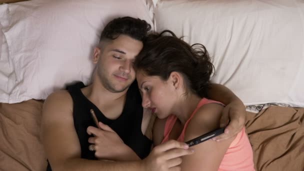 Couple addicted to social media networks spending time in bed together hugging and texting everyone on their smartphones — Stock Video