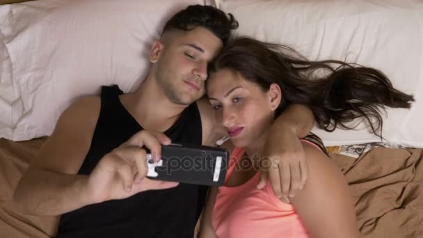 Chill teenage couple laying in bed and watching a movie on smartphone and having a lot of fun — Stock Video