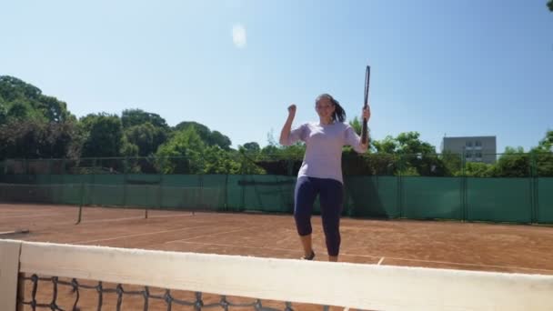 Победительница теннисной игры приходит к филе смеясь счастливо держа ракетку — стоковое видео