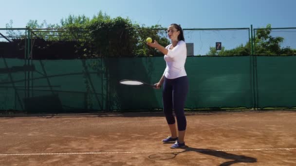 Mujer joven golpea la pelota de tenis con raqueta en la cancha de tenis — Vídeos de Stock