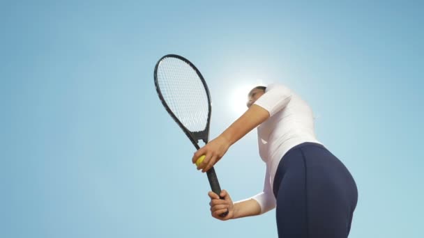 Menina bonita jogador de tênis mulher servindo bola com raquete ao ar livre com sol atrás dela — Vídeo de Stock