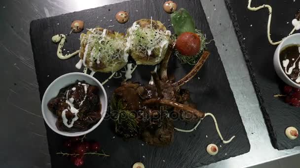 Sofisticado y sabroso menú con carne de cordero adornada con salsa y verduras en un plato de servir negro en una cocina de restaurante — Vídeo de stock