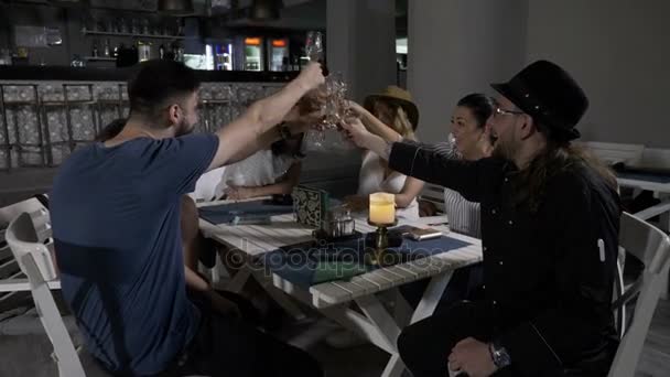 Grupo de felices amigos de los millennials sentados a la mesa en el salón del restaurante brindando y tomando copas — Vídeos de Stock