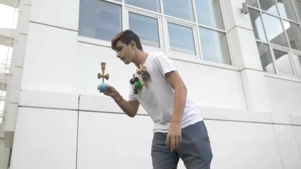 Movimiento lento del joven que ejerce el equilibrio fronterizo truco kendama al aire libre en el patio de la escuela — Vídeos de Stock