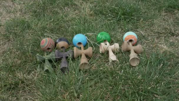 Nahaufnahme von Jungen, die sich jeweils ein kendama-Spielzeug aus dem Gras zum Spielen aussuchen — Stockvideo