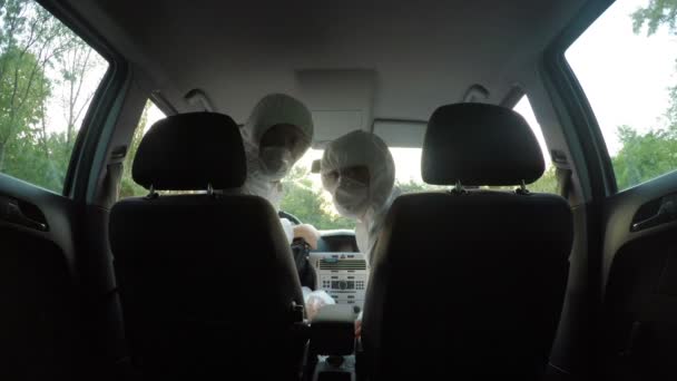 Young biohazard scientists technicians colleagues in hazmat suits in car turn looking at the backseat of the car — Stock Video