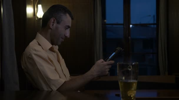 Человек сидит за столом в баре и улыбается и держит планшет в руках — стоковое видео