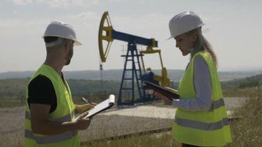 Çekici kadın mühendis ve foreman konusunda konuşurken iş çizelgesi yakınındaki bir petrol pompa birimi