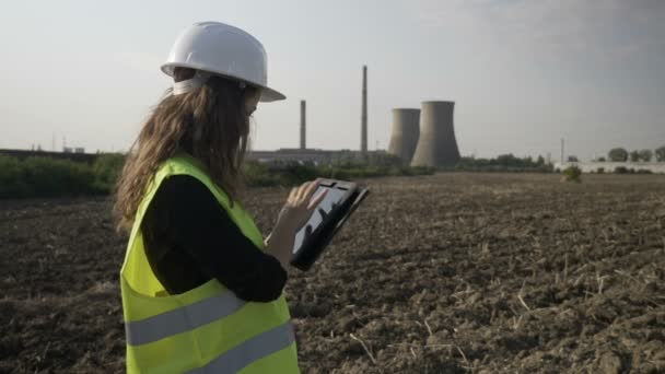 Hermosa joven especialista ingeniero femenino comprobar y calcular con dispositivo electrónico tableta pc datos de contaminación ambiental cerca de la refinería de petróleo — Vídeo de stock