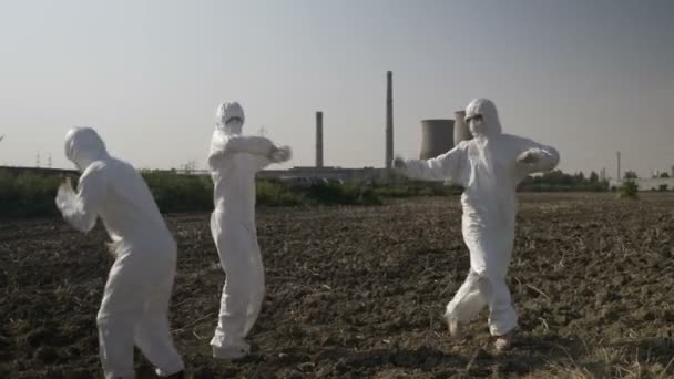 Grappige wetenschappers in hazmat pakken dansen en rotzooien rond in de buurt van de locatie van een raffinaderij vieren succesvolle corona virus covid-19 missie — Stockvideo