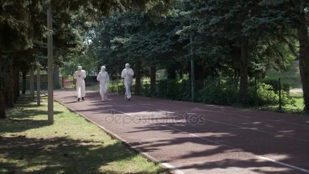 Трое мужчин в защитных костюмах бегут по курсу в парке — стоковое видео