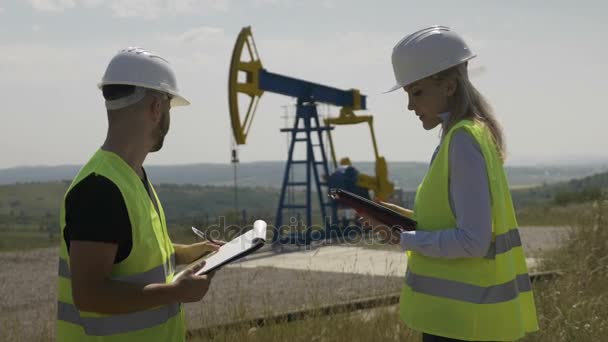 Attractive female engineer and foreman discussing about work schedule near an oil pumping unit — Stock Video