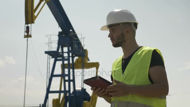 Ingeniero joven confiado analizando el calendario para el procesamiento de la actividad petrolera en su tableta — Vídeo de stock