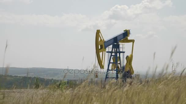 Нефтяной насос работает на пшеничном поле с холмами на заднем плане — стоковое видео