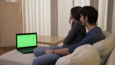 Mutlu çift evde gülme ve iyi vakit geçiren yeşil ekran ile bir dizüstü bilgisayar bir komedi film izlerken
