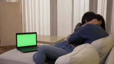 Evli çift yaşayan, Oda sarılma ve gülüyor yeşil ekran ile bir dizüstü bilgisayar üzerinde bir gerilim film izlemek